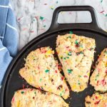 bottom right vanilla scones in triangle shapes with funfetti in it. Placed in a black pan and a blue towels with white line ons the right