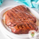 Whole top round steak seared and still juicy, sitting on serving plate.