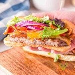 Two burger dogs fully load, one on a serving board the other held above it.