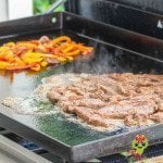 Grilling the flank steak slices for fajitas on the griddle with the onions and pepper mixture keeping warm on the opposite side.