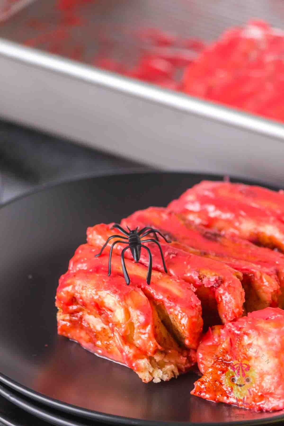 Halloween cinnamon roll intestines on a black plate with a toy spider on top. The magic of this recipe is way beyond the ingredients. It is fun and creative, a conversation stater, customizable, and a fun dessert imposter.