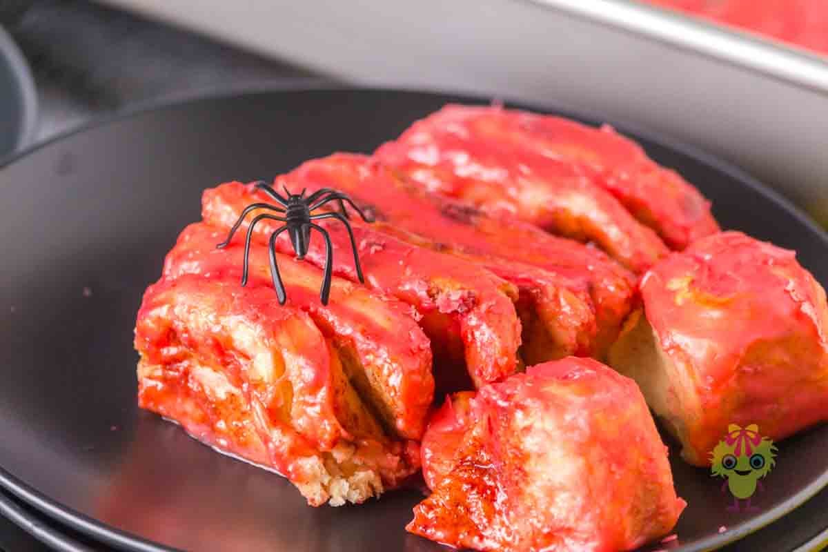 Halloween cinnamon roll intestines on a black plate with a toy spider on top. The magic of this recipe is way beyond the ingredients. It is fun and creative, a conversation stater, customizable, and a fun dessert imposter.