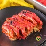 Halloween cinnamon rolls shaped like intestines on a black plate with toy spiders. The red icing adds the perfect touch of gore.