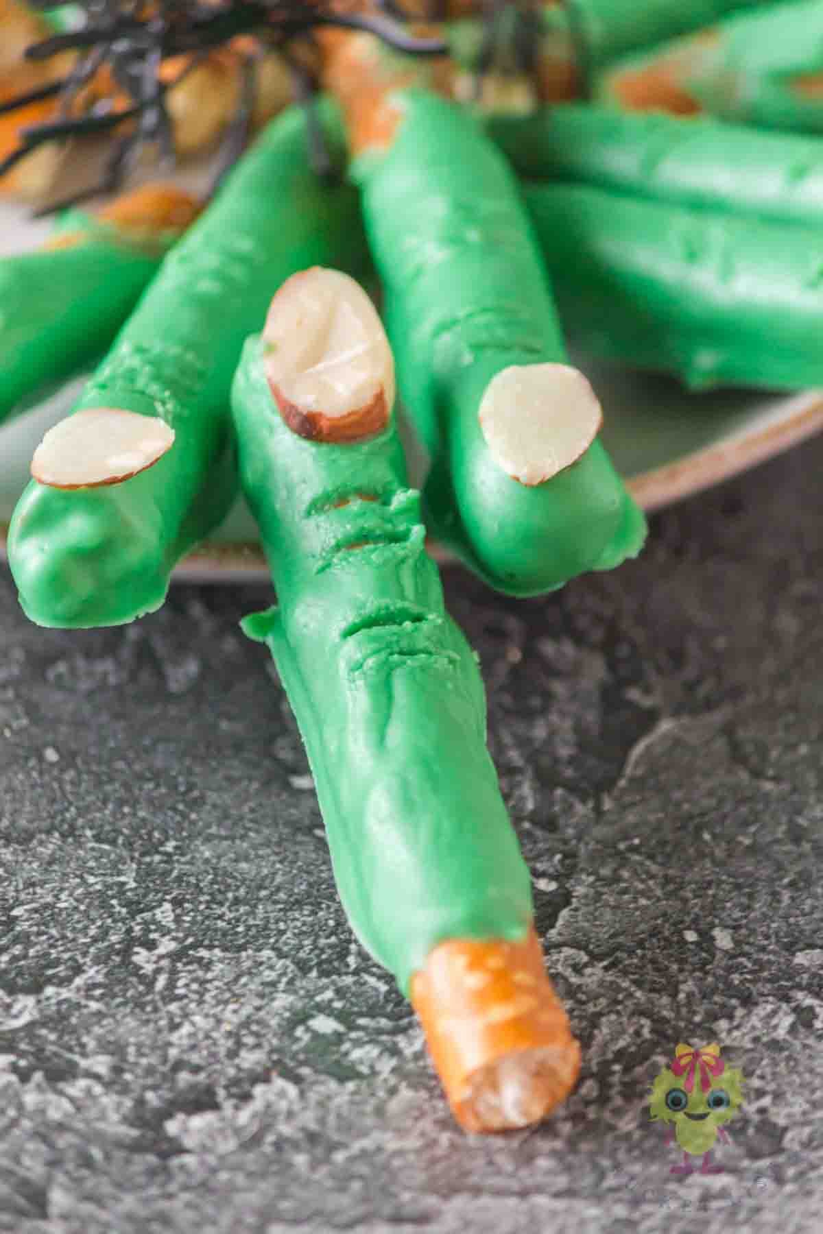 Showing the Halloween pretzels shaped into witch fingers pretzels with just 3 ingredients. Using candy melts to coat the pretzel rods is a game-changer to shape the fingers.