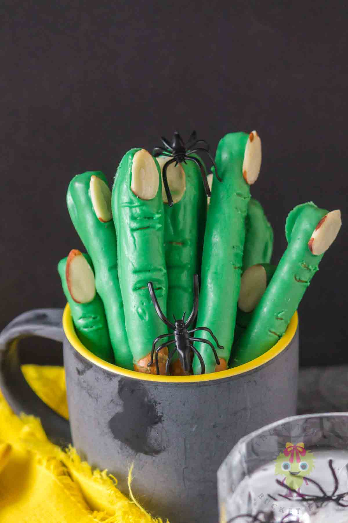 Halloween pretzels decorated as witch fingers with toy spiders crawling on them. Placed in a spooky black cup.
