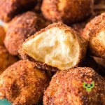 A pile of cinnamon sugar donut holes with one that has a bite taken out of it, showing the cinnamon crust.