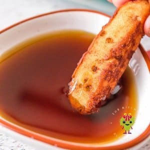 A golden crisp Pillsbury cinnamon stick fresh from the air fryer being dipped in maple syrup.