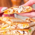 Holding a piece of the crispy bacon chicken ranch quesadilla with meted cheese and a drip of ranch dressing coming from the middle. It is ready to be eaten.