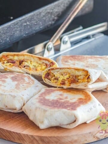 Four Taco Bell breakfast crunchwraps on a wooden cutting board, browned perfectly, with one cut in half. You can see how the hashbrown is crispy, the cheese is melted, and everything looks so fresh.