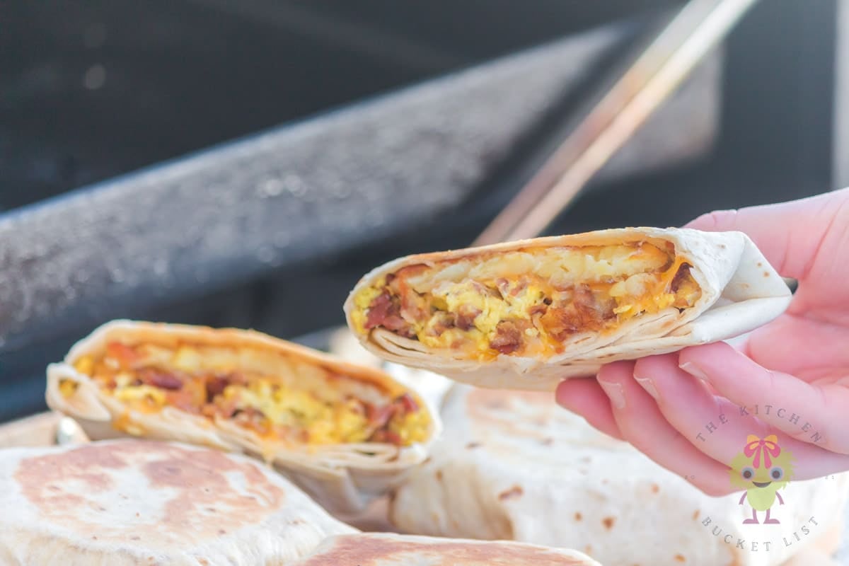 Four Taco Bell breakfast crunchwraps on a wooden cutting board, with one cut in half. One-half is held above the others. The hashbrown is crispy, the cheese melted, and everything looks so fresh.