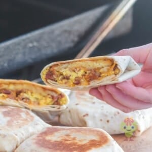 Four Taco Bell breakfast crunchwraps on a wooden cutting board, with one cut in half. One-half is held above the others. The hashbrown is crispy, the cheese melted, and everything looks so fresh.