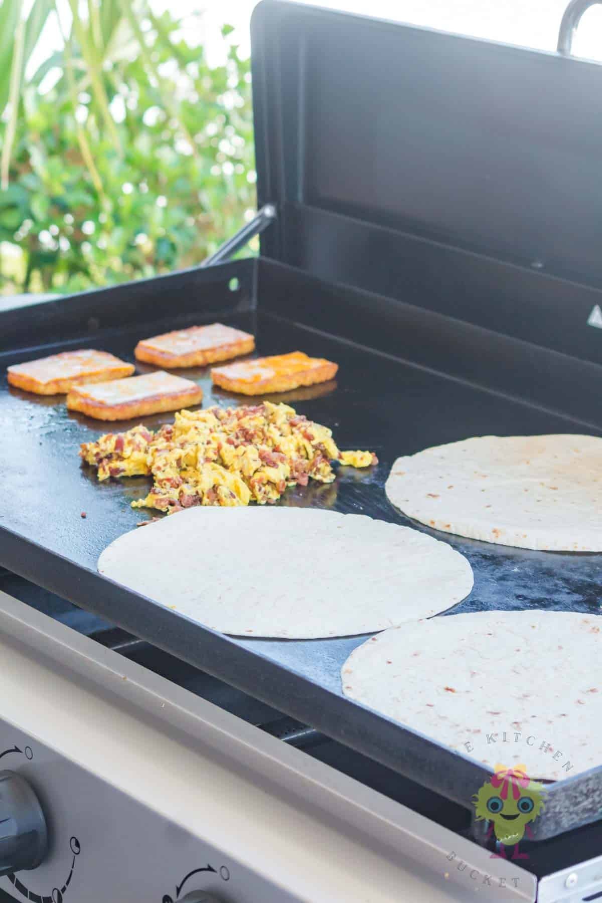 All the ingredients are ready to assemble the breakfast crunchwraps. Hashbrowns are golden crisp with cheese melting, eggs scrambled with bacon, and tortillas are warmed.