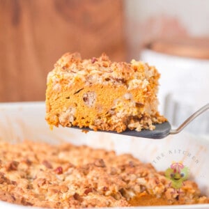 A piece of pumpkin pie cake with its warm pumpkin spice creamy pie-like filling and crunchy golden buttery topping. It is being served from the 9x13 dish, which makes it the perfect make-ahead cozy fall dessert.