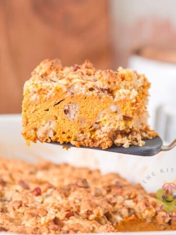 A piece of pumpkin pie cake with its warm pumpkin spice creamy pie-like filling and crunchy golden buttery topping. It is being served from the 9x13 dish, which makes it the perfect make-ahead cozy fall dessert.