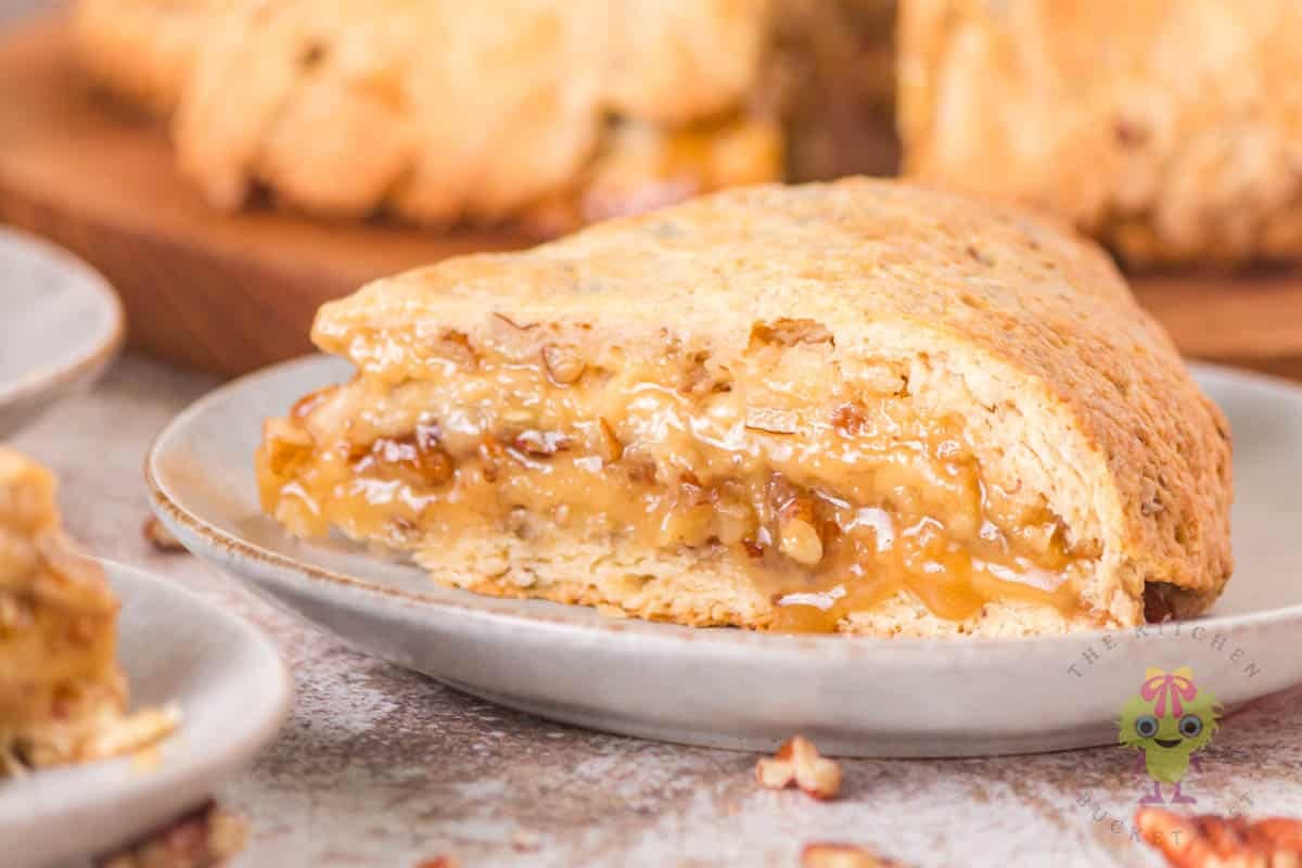 Pecan pie scone on a plate ready to enjoy. It has a perfect golden crust and in the middle is the pecan pie filling.
