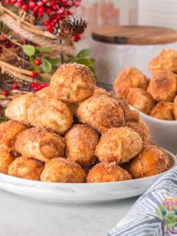 Golden, soft pretzel bites stacked on a serving plate with a festive holiday setting behind them.