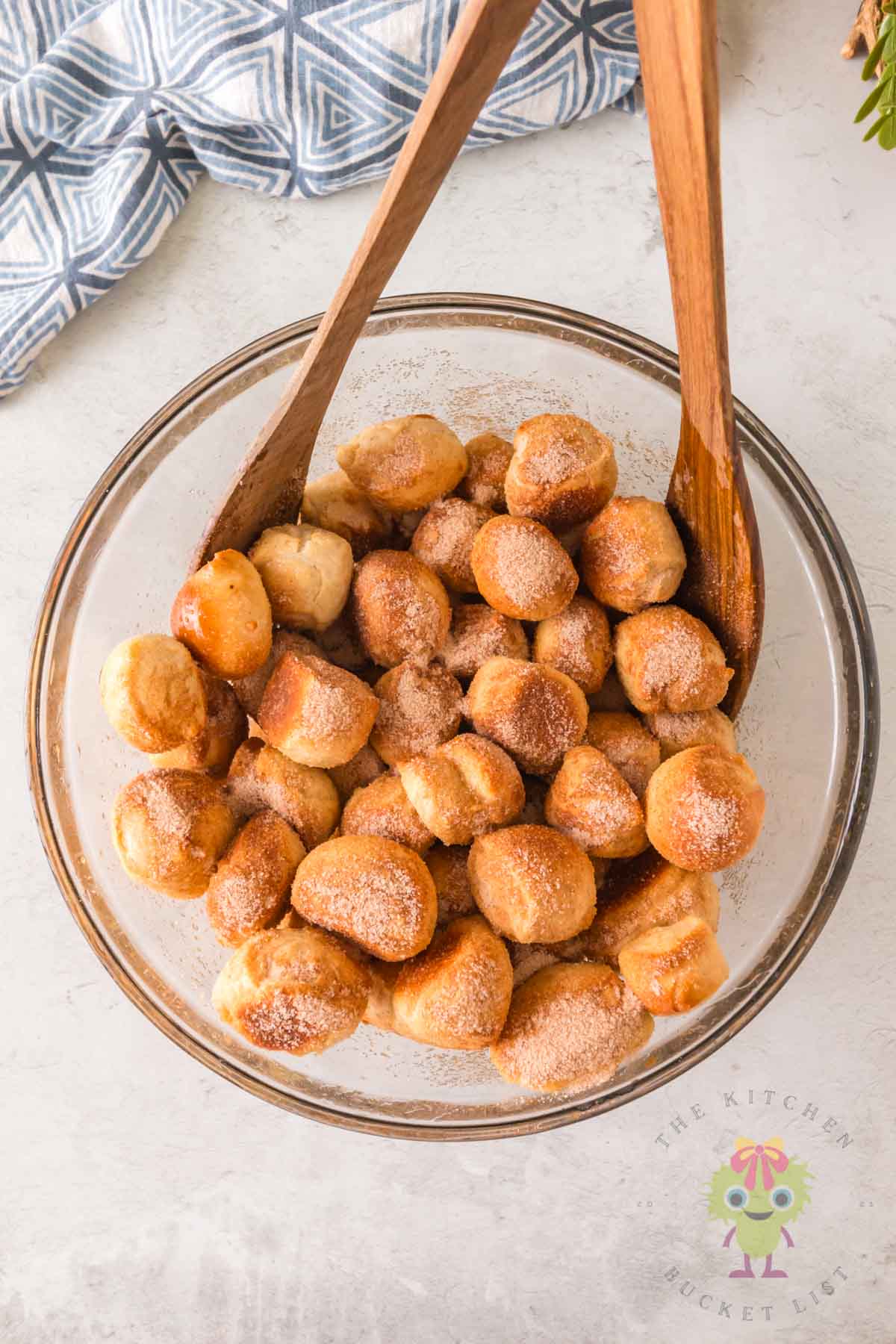 Wooden spoons stirring golden baked pretzel bites with cinnamon sugar in a large bowl.