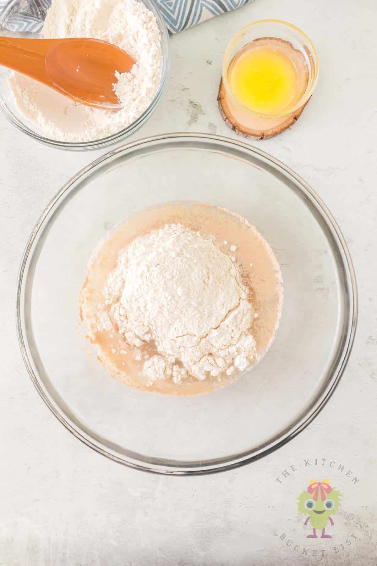 Wet and dry ingredients in a mixing bowl with warm melted butter and half the flour measured in separate bowls, ready to begin the dough
