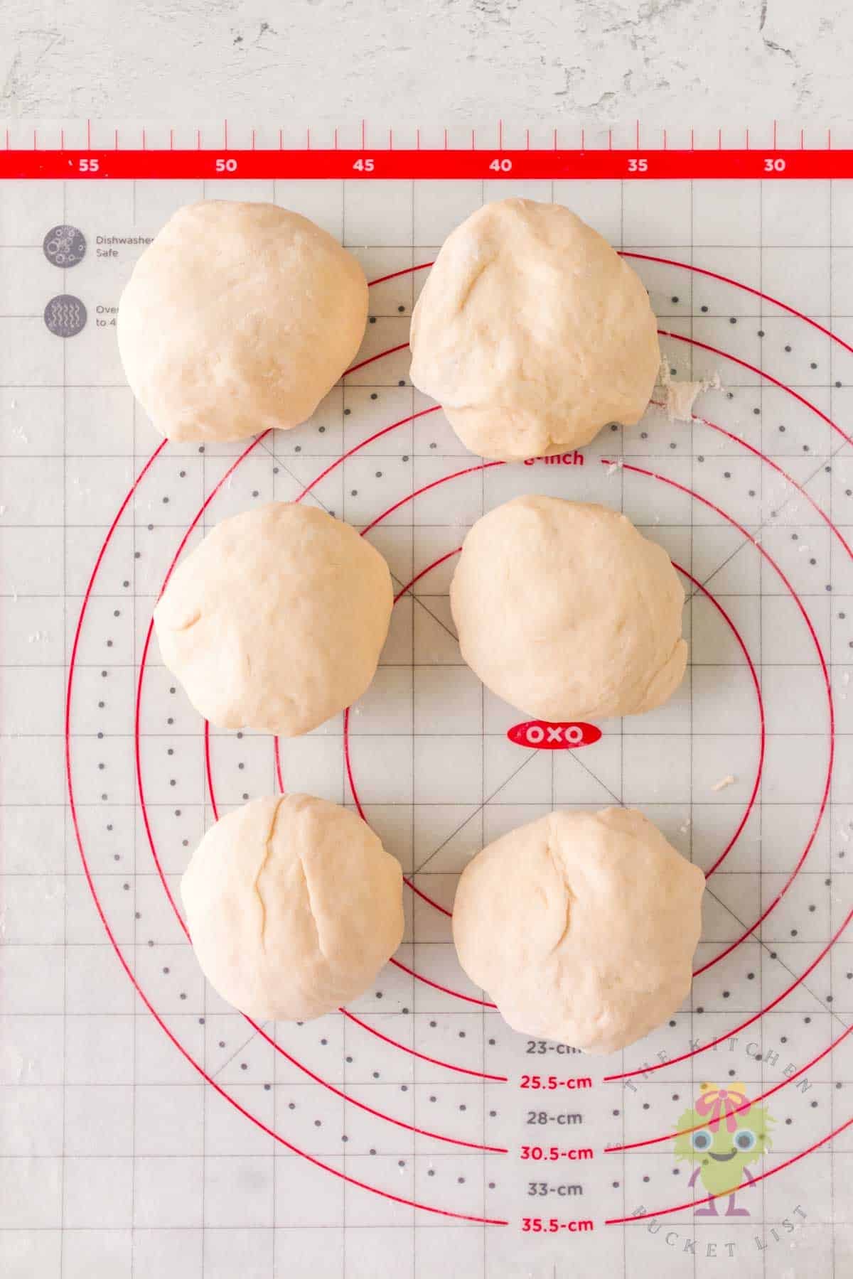 Overhead view of six dough balls on a work surface, ready to be rolled into ropes for cutting into bite-sized pieces.