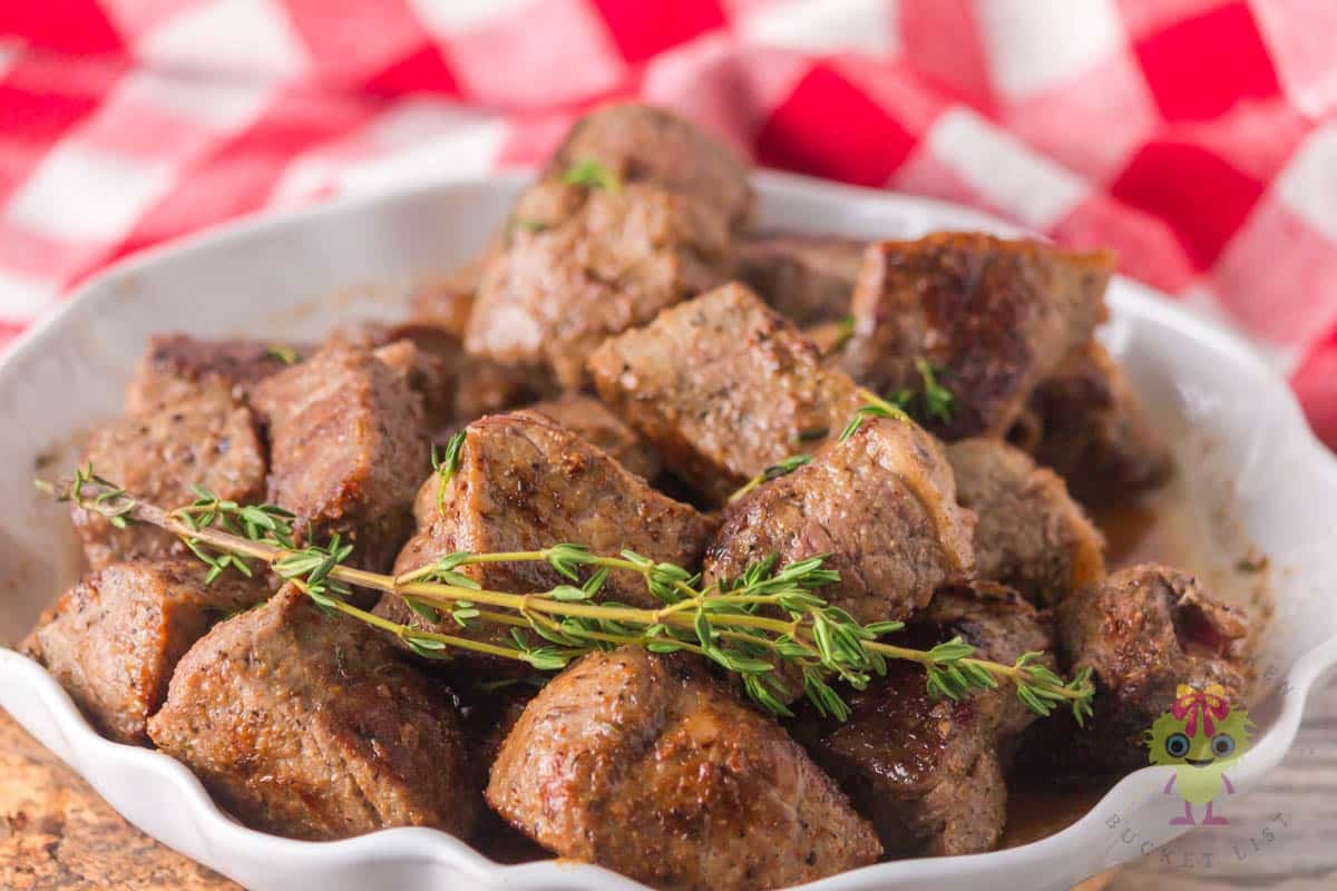 The garlic steak bites are in a serving bowl with a sprig of thyme and parsley sprinkled on top. You can see how tender the NY strip steak bites are after the hot and fast sear on the griddle. The dry rub with simple pantry spices and the finish with rich garlic butter makes them a true steakhouse treat right at home.