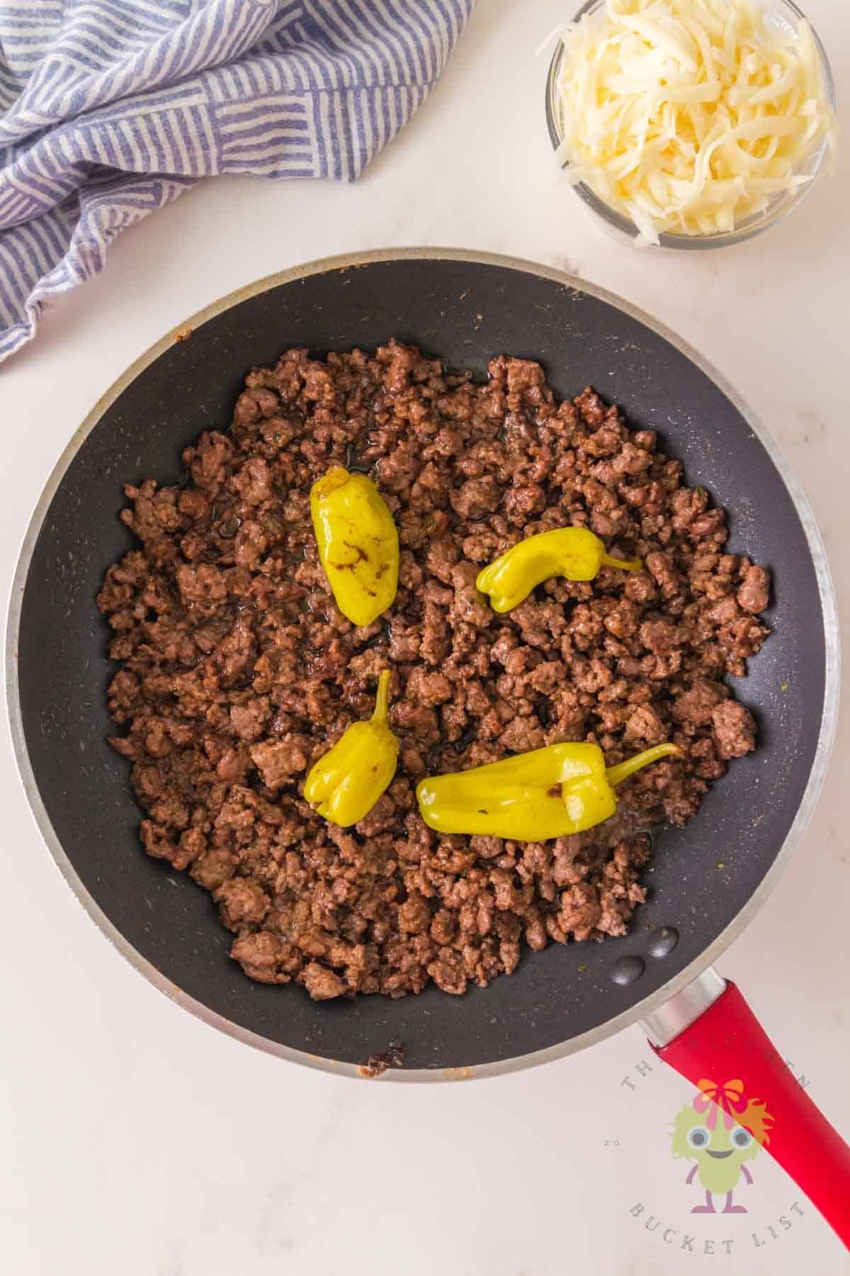 Cooked ground beef in a skillet mixed with whole pepperoncini peppers and seasonings for Mississippi quesadillas.