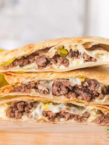 Stack of sliced air fryer Mississippi ground beef quesadillas on a wooden cutting board showing the cheesy beef filling with pieces of pepperoncini.